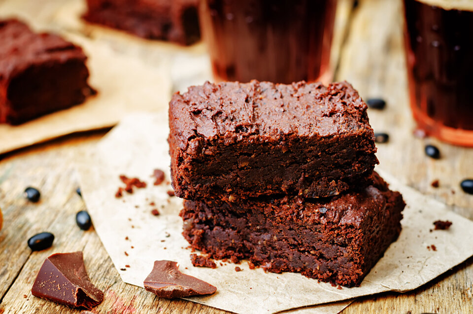 Brownies met zwarte bonen en dadels Blokje bruine brownie op een wit papiertje met snippers chocolade ernaast
