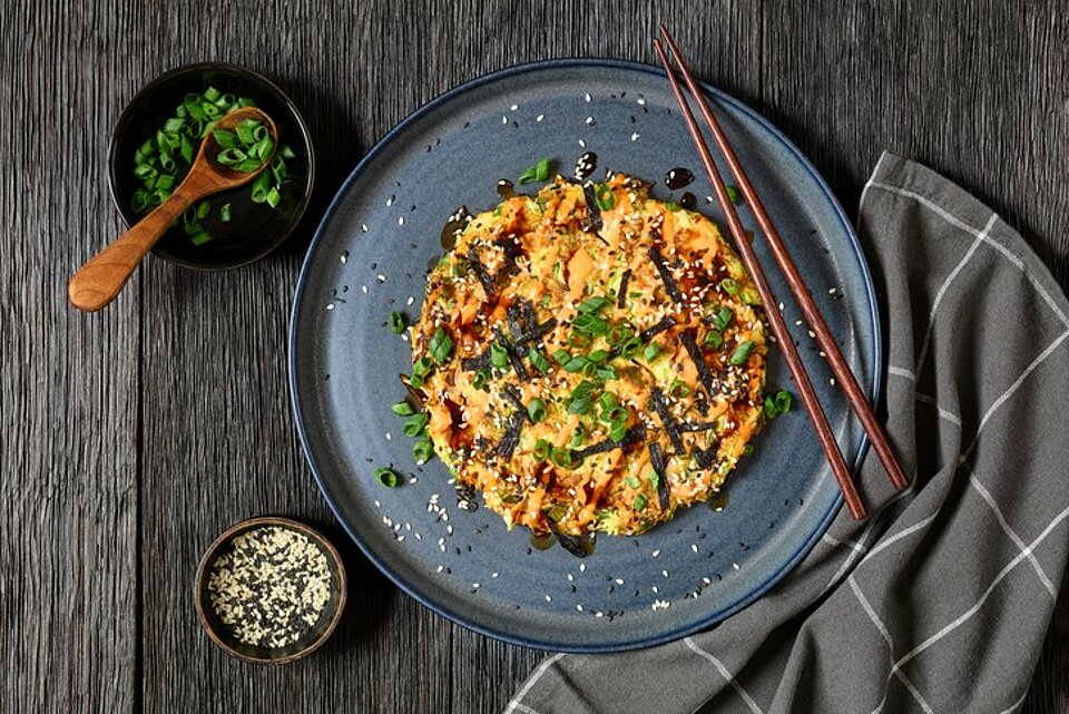 Okonomiyaki - Japanse pannenkoek Bord met een met groenten gevulde pannenkoek op een donkeler Japans uitziende) tafel