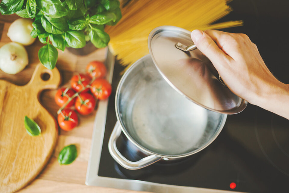 11 tips om milieuvriendelijker te koken koken met deksel op de pan naast een plank met tomaten en kruiden